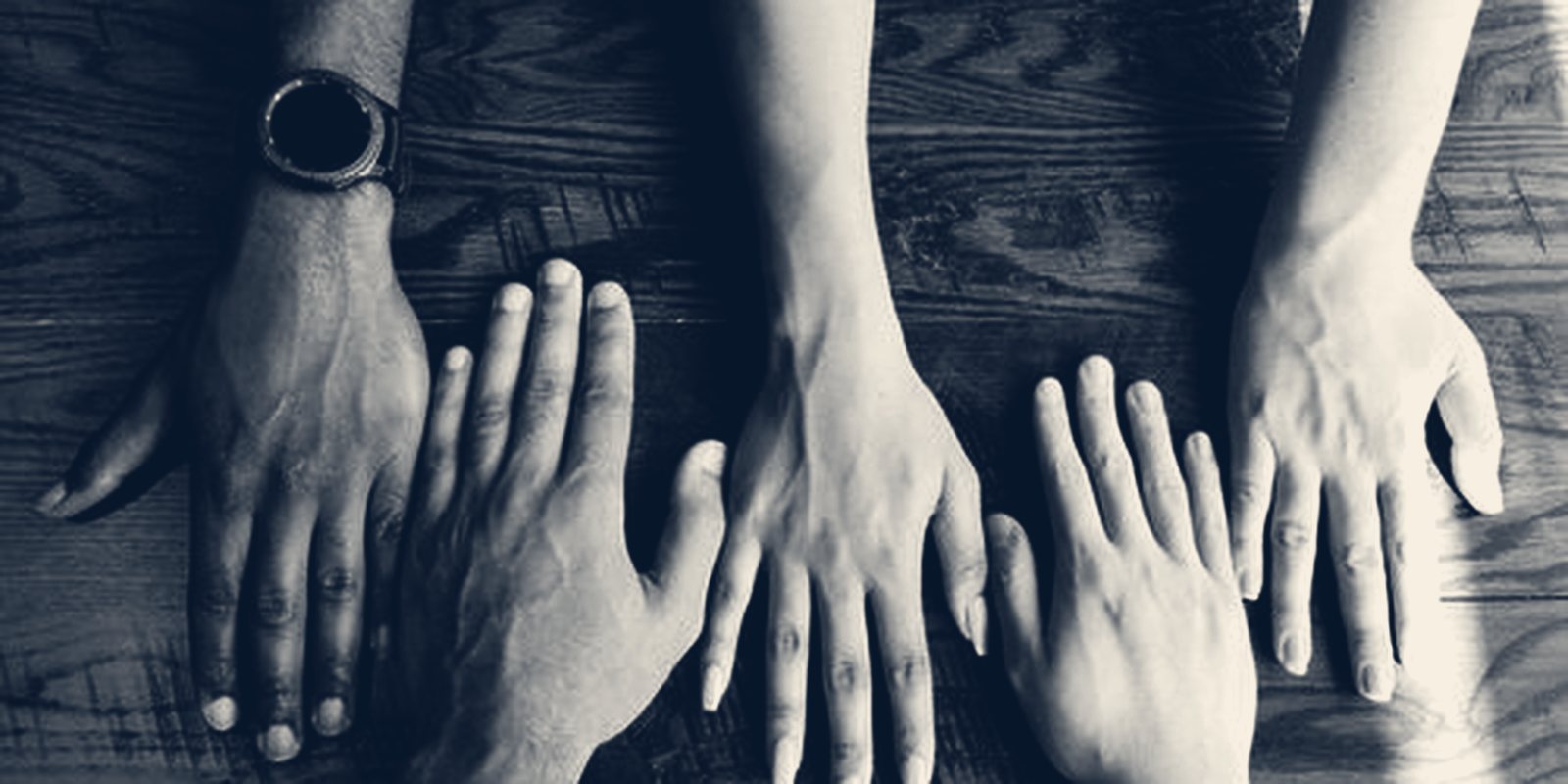 The hands of several people laid side by side on a dark wooden table