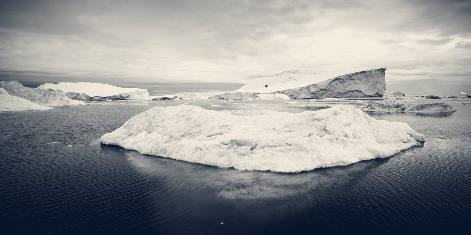 An iceberg floating on still, dark water under an overcast sky