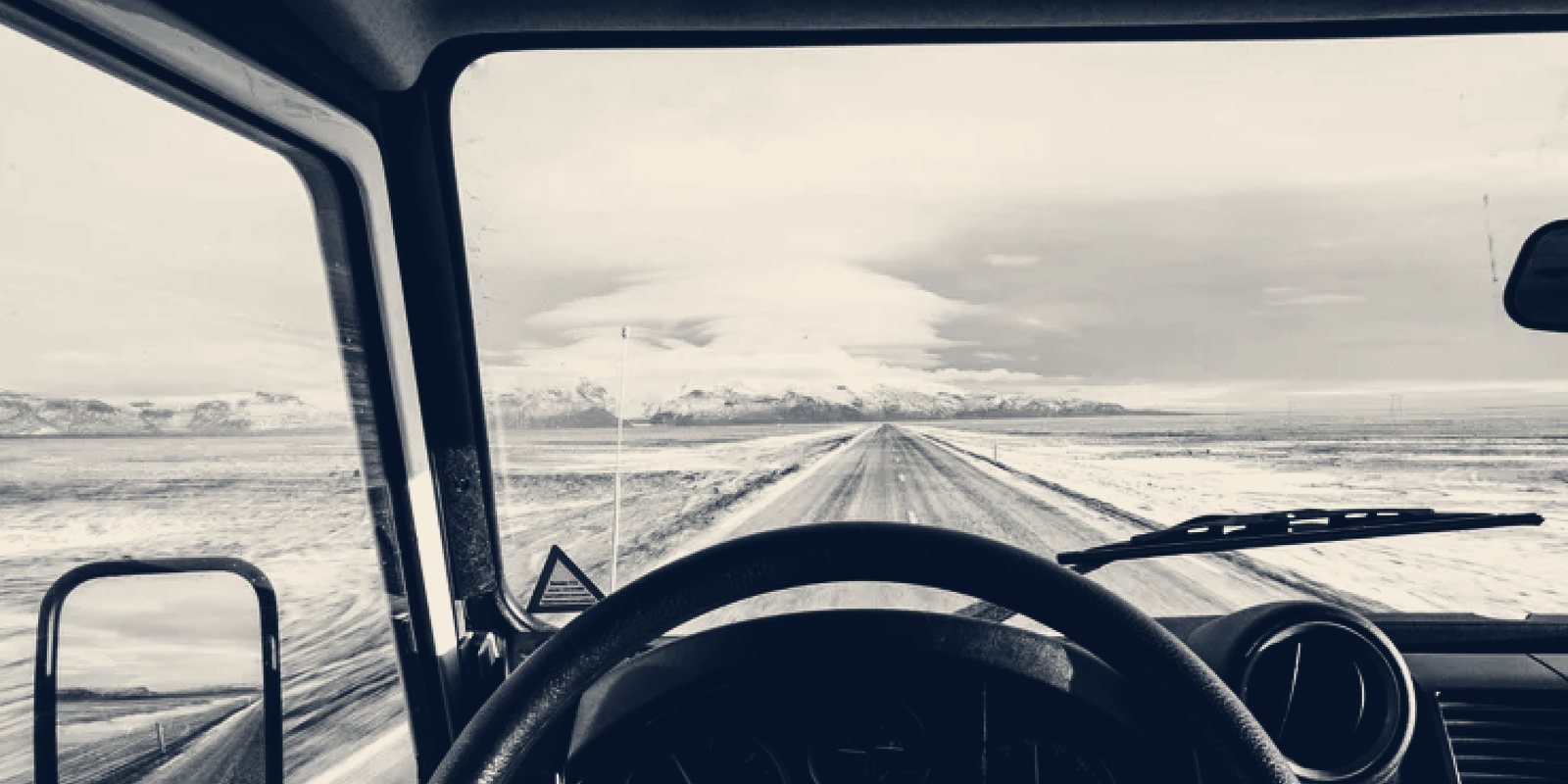 The view over a steering wheel of a straight, empty road running toward distant mountains