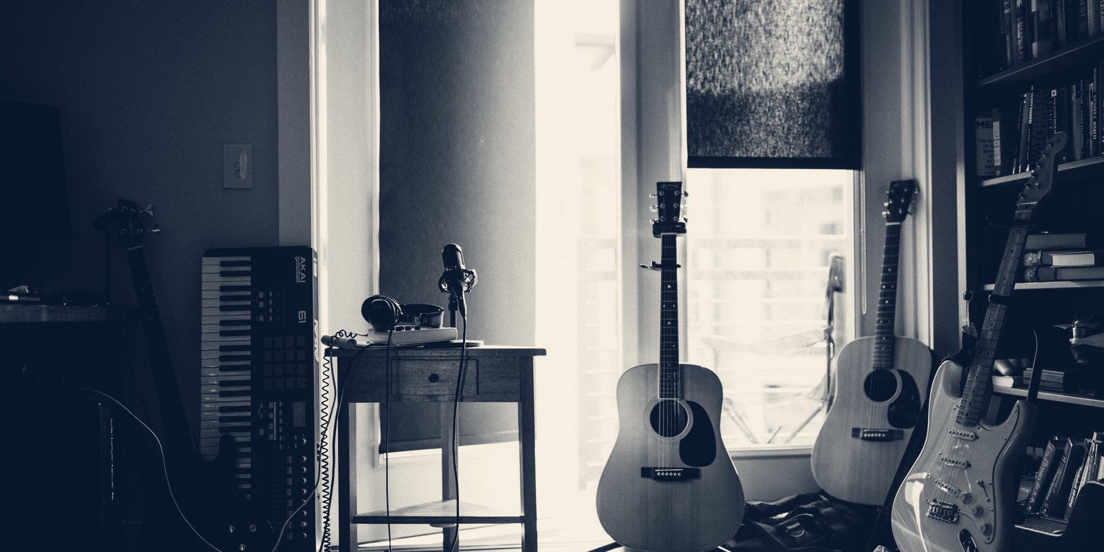 A home music corner with a keyboard, a microphone on a small desk and three guitars by a window