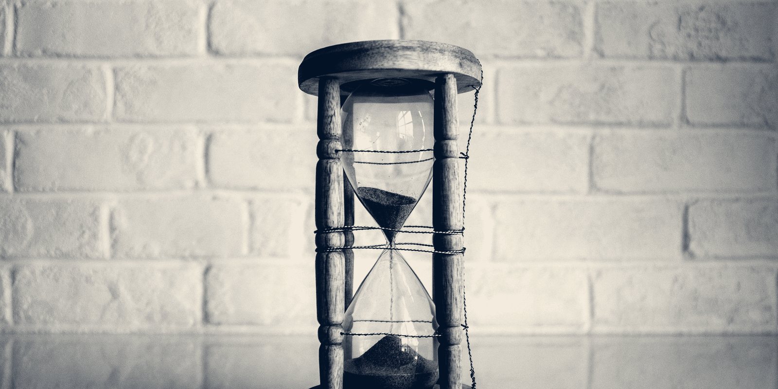 An hourglass with sand running through it, in front of a white brick wall