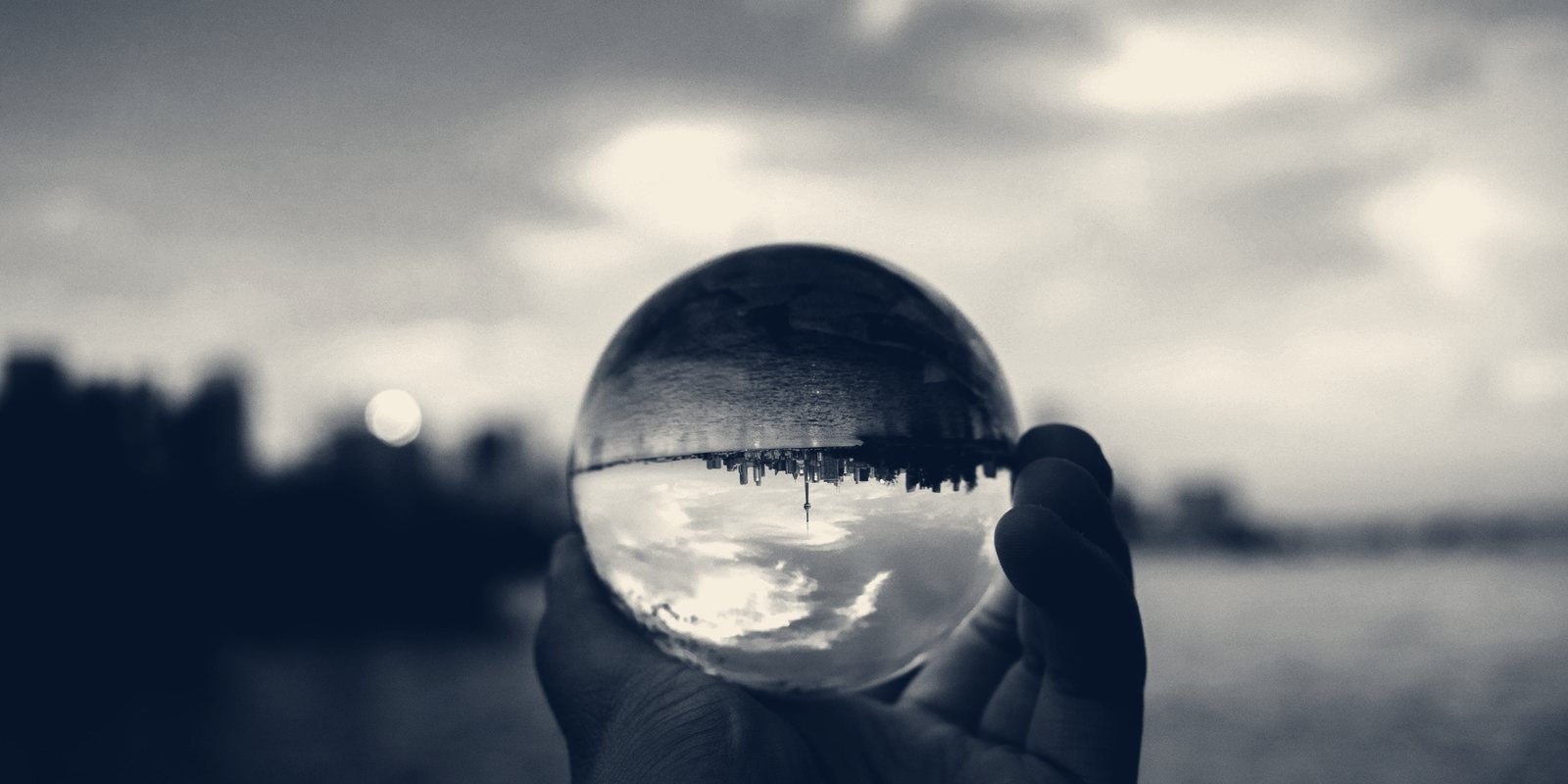 A hand holding a glass ball that shows the skyline and the sky upside down