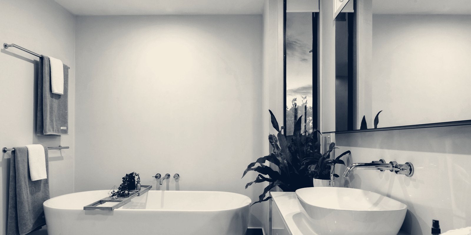 A bathroom with a freestanding bathtub, a basin, towels on rails and a potted plant
