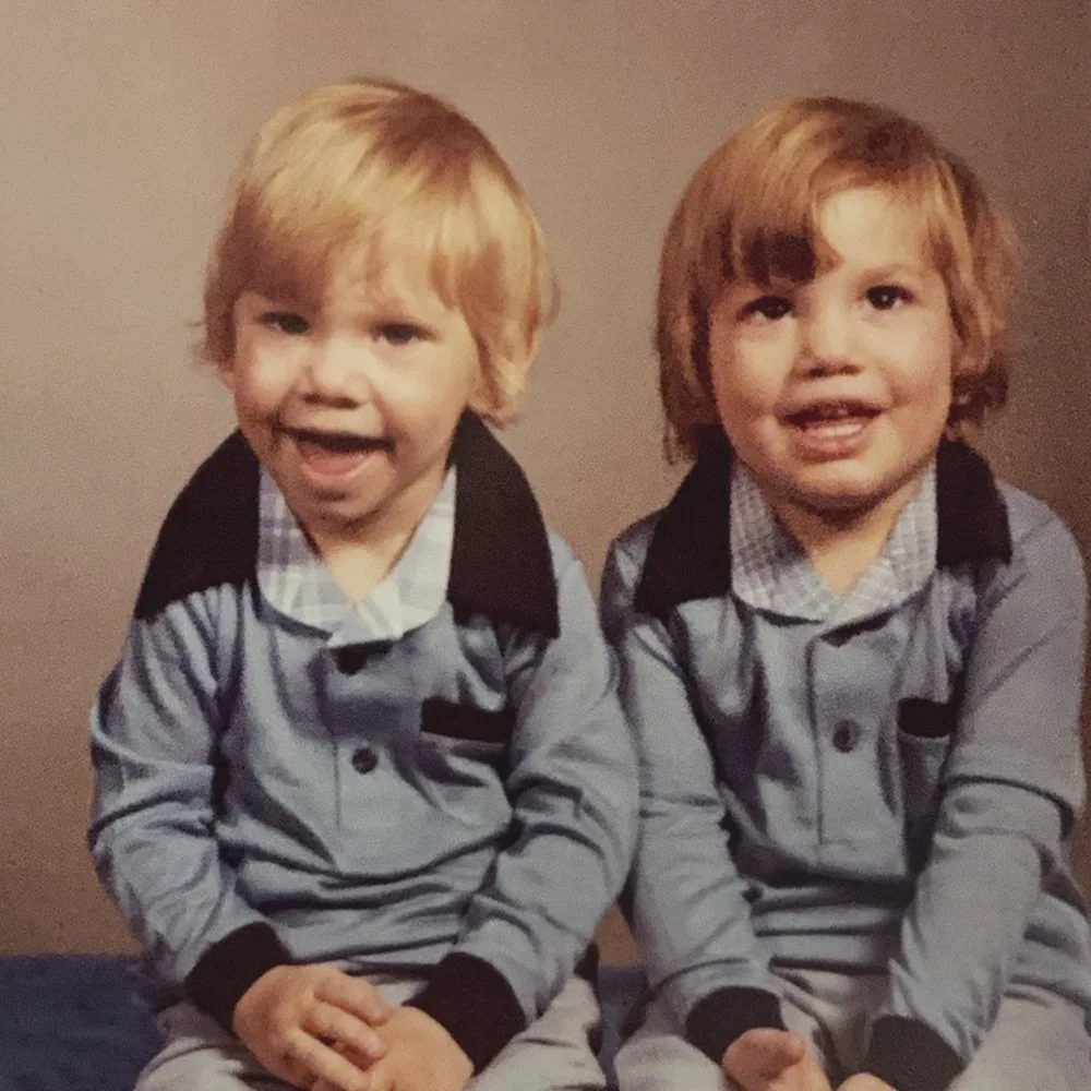 Two toddlers in matching blue outfits sitting side by side for a studio portrait