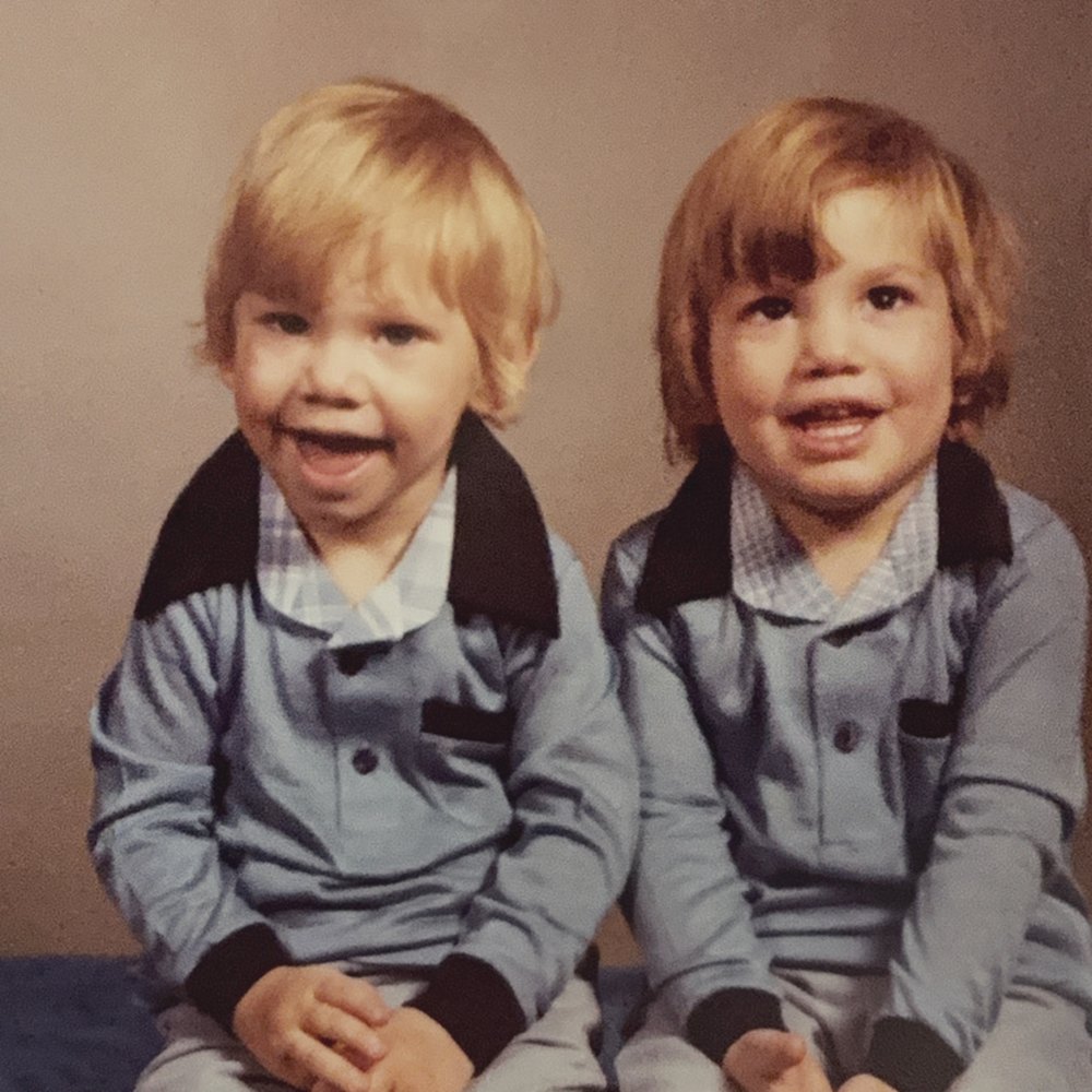 Two toddlers in matching blue outfits sitting side by side for a studio portrait