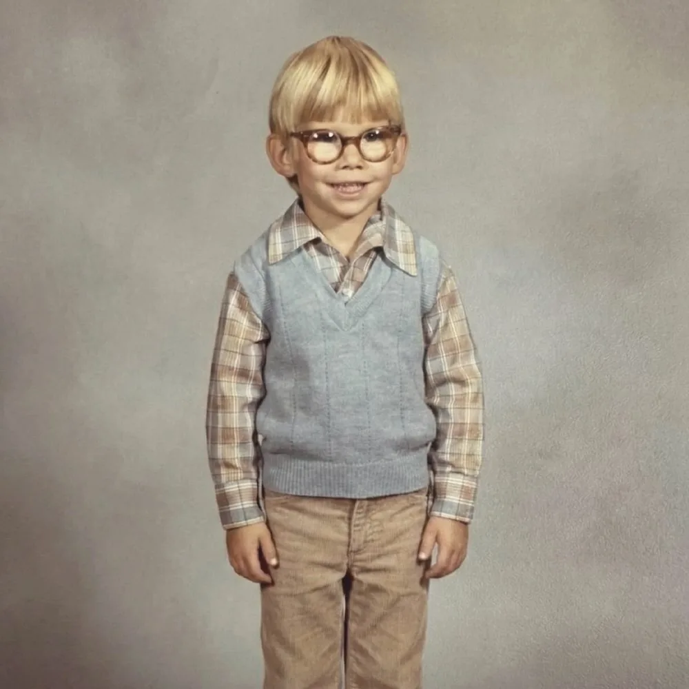 Studio portrait of a young boy in glasses, a plaid shirt and a blue sweater vest