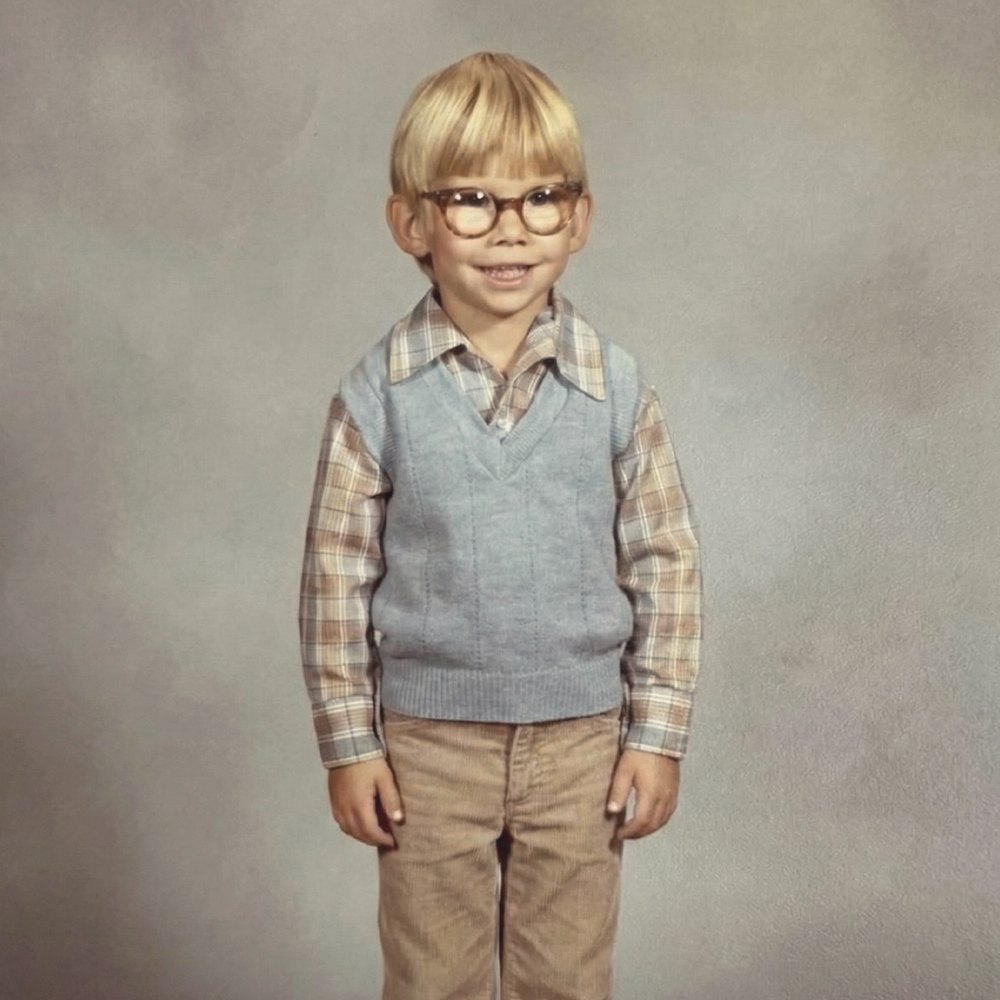 Studio portrait of a young boy in glasses, a plaid shirt and a blue sweater vest