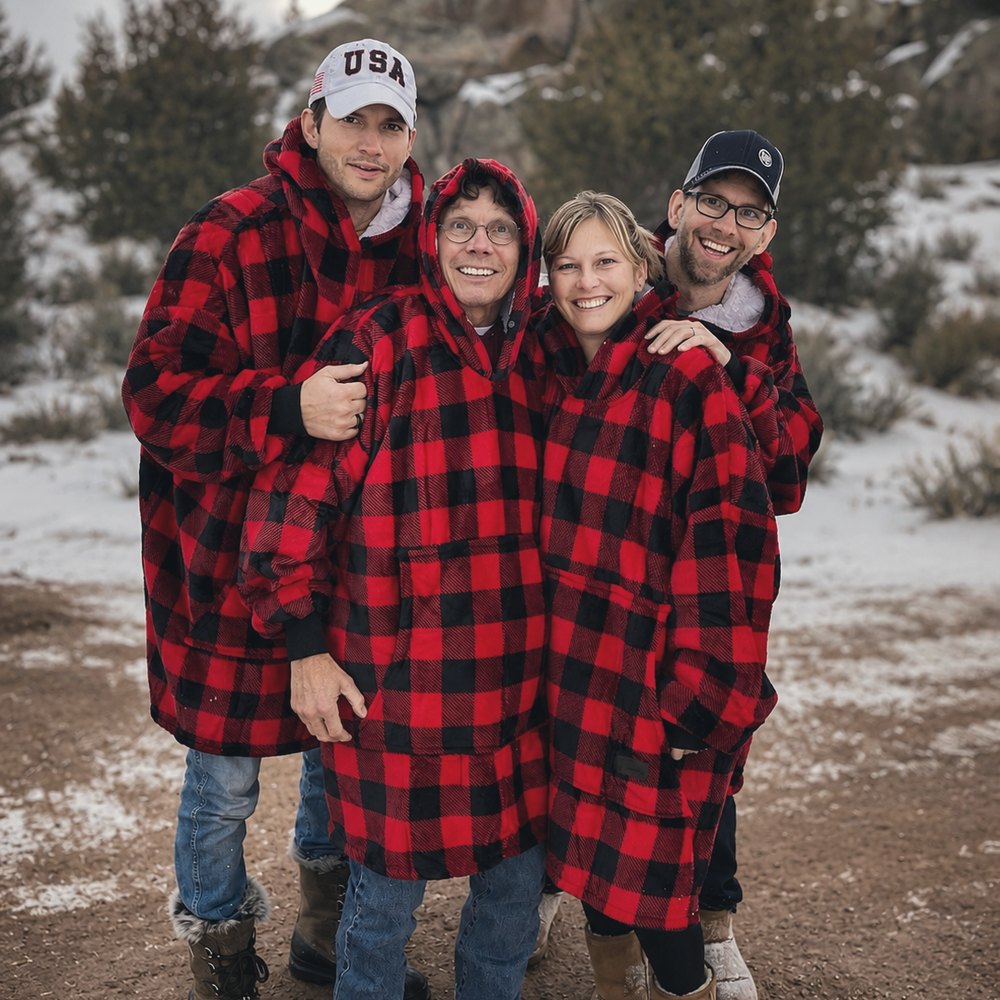 Four adults in matching red and black plaid hooded robes, arm in arm on a snowy hillside